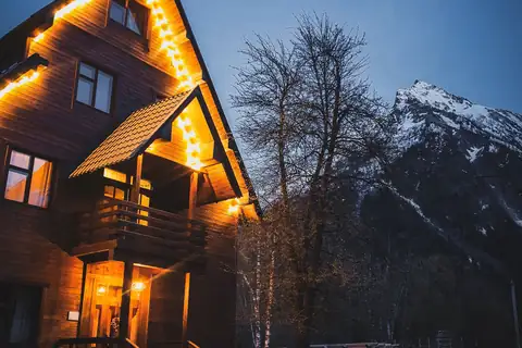 Mountain chalet with warm glowing lights at dusk below snowy peaks