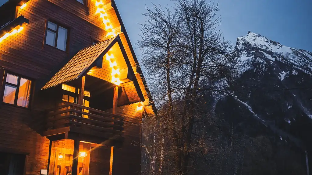 Mountain chalet with warm glowing lights at dusk below snowy peaks